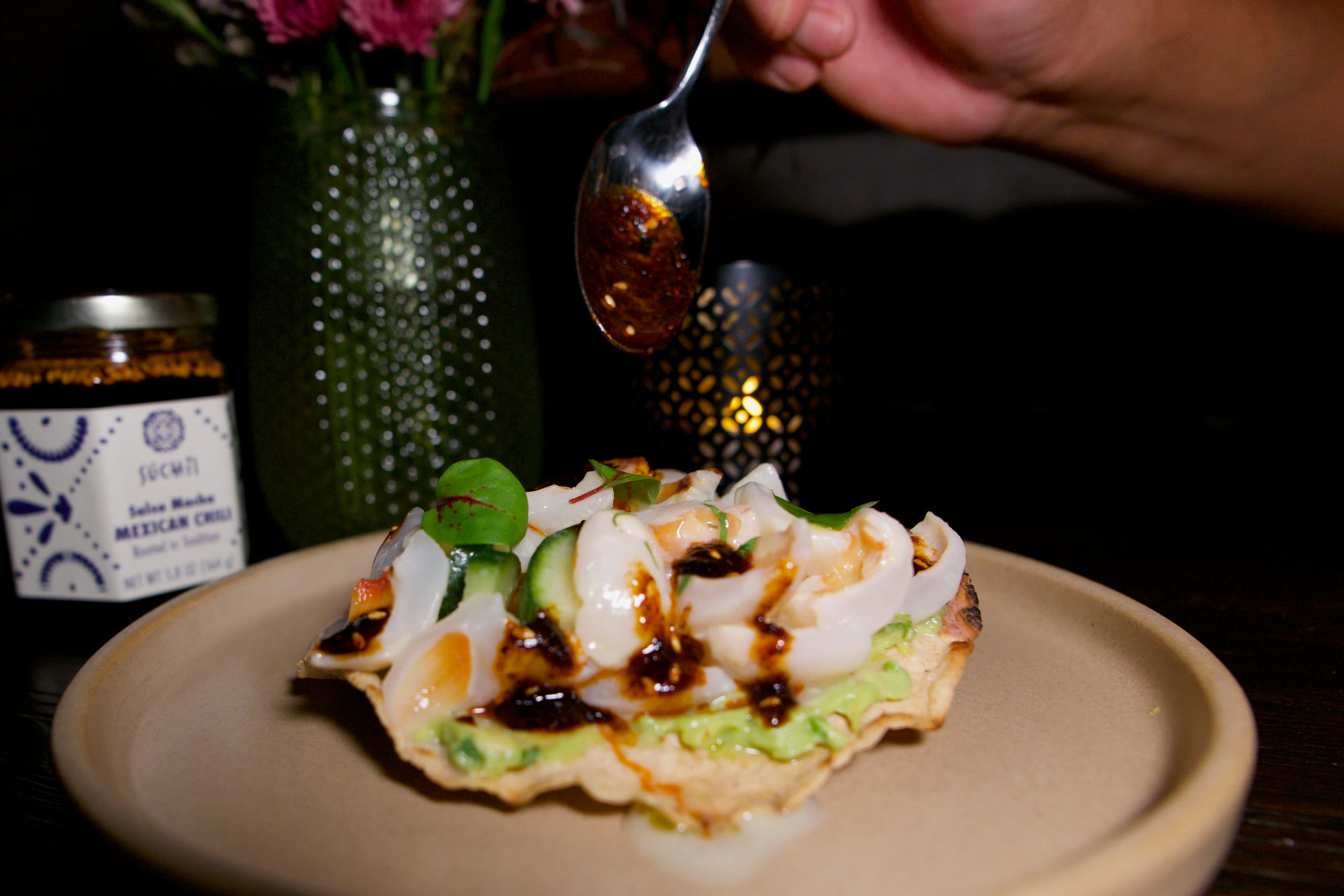 Salsa macha spooned over a tostada with a Súchil Made jar in the background.